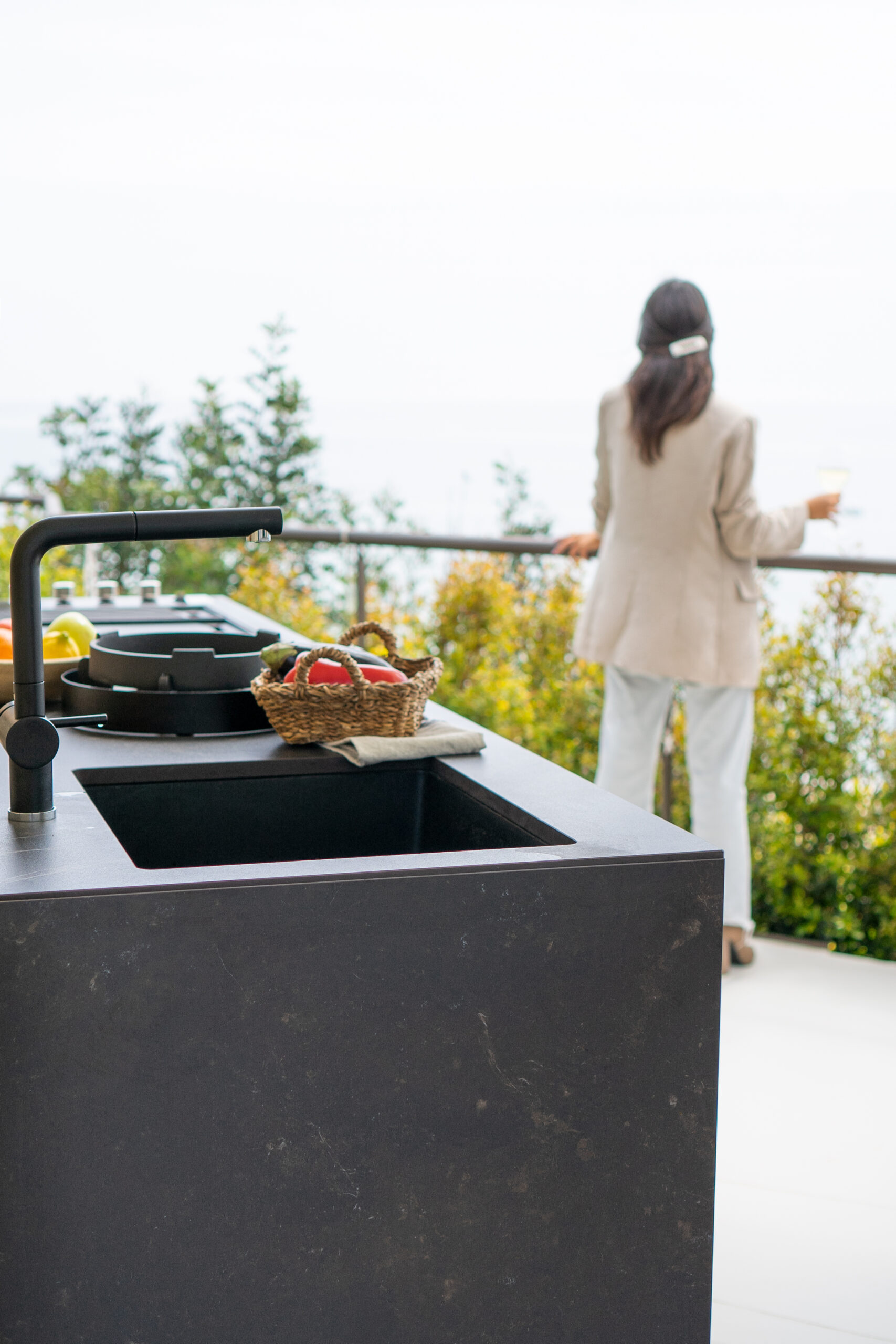 Une femme qui regarde un jardin à coté d'une cuisine d'extérieur